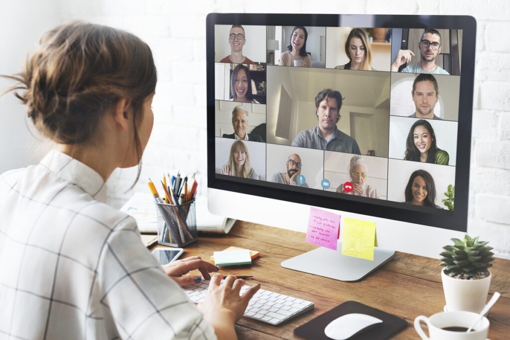 Woman at home desk looking at a screen showing many online meeting attendees.